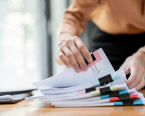 Businesswoman,Hands,Working,In,Stacks,Of,Paper,Files,For,Searching